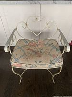Front view of metal wide frame chair with heart shaped backrest and floral seat cushion showing wear and discoloration.