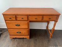 Front view of a hardwood desk showing four drawers with two smaller drawers on top left and right, two larger drawers on left bottom, turned legs on right, with scuffs and scratches visible on surface.