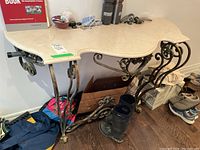 Photo showing angled view of entry table with curved beveled faux marble top and ornate metal base with leaf motifs.