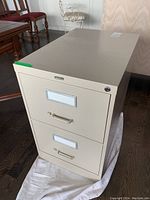 Front view of beige 2 drawer metal filing cabinet showing label holders, metal handles, and lock on top drawer.