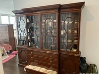 Front view of the wood hutch showing glass front doors with decorative wooden grid trim, metal pulls, and contents inside the glass enclosure.