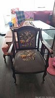 Front view of antique wood framed armchair with needlepoint floral upholstery on seat and backrest