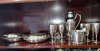 Shelf with six silver plate wine goblets, cocktail shaker, ice bucket, and two covered serving dishes