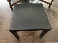 Top view of the black Ikea Lack side table showing square surface and four legs on wood flooring. Surface has visible scuff marks.