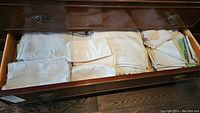 Drawer filled with various folded vintage table linens including napkins and tablecloths in different colors and sizes.