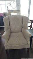 Front view of the beige upholstered wing back armchair showing the seat cushion and wingback design.