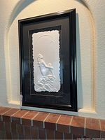 Full view of framed white cast paper relief artwork depicting a nude woman sitting on rocks with crescent moon overhead, mounted in black frame.
