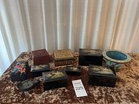 Collection of Asian-style lacquered boxes, carved wooden box, porcelain pot, and small metal item arranged on brown velvet surface