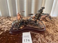 Full view of the bronze sculpture showing a cowboy on horse chasing a steer on a wooden base