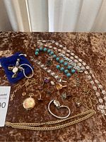 Photo showing assorted costume jewelry including necklaces, rings, bracelets, a pocket watch pendant, and cufflinks arranged on a brown velvet surface.