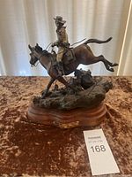 Full right-front view of the bronze sculpture showing cowboy on horse and wooden base