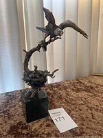 Full view of sculpture showing eagle with wings spread perched on a branch over a nest with eaglets, mounted on marble base.