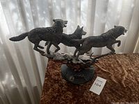 Full view of bronze sculpture showing three wolves in motion on rocky terrain with visible detail and texture.