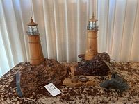 Overall view of two lighthouse lamps on burl wood bases alongside sailboat model, whale figurine, shell, and anchor sculpture