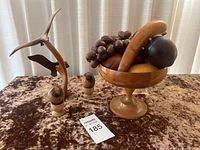 Wide view of all items showing wooden bowl with wood fruits, sculptural piece, and two bottle stoppers on velvet surface.