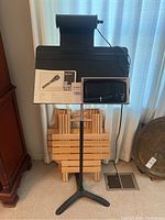 Full photo showing black music stand with a black music stand light and the microphone with the manual on the stand.