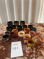 Front view of 18 assorted napkin rings showing various colors, materials, and decorative styles arranged on a brown patterned cloth.