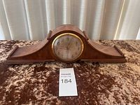 Front view of the Sentinel wooden mantle clock on a brown textured fabric background.