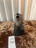 Front view of detailed wolf head sculpture on black base, showing open mouth and textured fur.