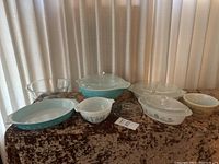 View of the full set of seven Pyrex glass bakeware pieces arranged on a brown textured cloth surface with a curtain in the background.