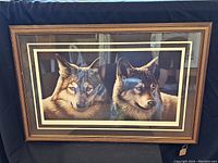 Front view of the framed print showing two wolves in realistic detail within a wooden frame with light and gold matting.