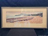 Full view of framed coastal landscape print showing the entire scene with beach, driftwood, grasses, distant trees and hills.