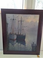 Front view of framed oil painting showing two sailboats at dock at dusk