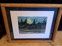 Full view of framed pastel drawing showing the artwork entitled "Moonrise" with moon and trees, in oak frame with white mat.