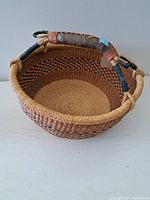 Angle view of the round woven basket showing the handle wrapped in leather and cords