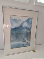 Framed watercolour painting showing a fishing boat on water with mountains in background. Signed by artist visible on bottom left.