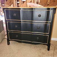 Front angle view of black French style dresser with gold trim and round black drawer pulls. Shows the decorative design and condition.