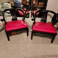 Pair of black lacquered Ming style Asian accent armchairs with red seat cushions shown side by side on beige carpet with mirrored wall in background