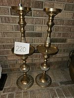 Pair of large brass candlesticks standing side by side showing their height and design.
