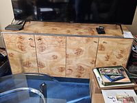 Front view of 4-door burl wood credenza with TV on top, showing wood grain patterns and black trim.