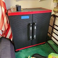 Front view of the red and black storage cabinet in a garage setting showing two doors with handles, red top and base trim, and hexagonal pattern on front panels.