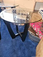 Three pieces: one large oval coffee table and two smaller round side tables, all with clear glass tops and black wood bases accented with metal.