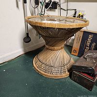 Side view of the round wicker side table showing woven wicker base and glass top.