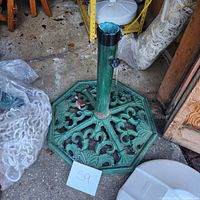 Front and top view of the heavy iron outdoor umbrella stand base placed on concrete floor showing green paint and decorative cut-out pattern.