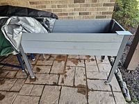 Front view of the large gray wooden planter on caster wheels, positioned on outdoor stone paving.
