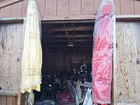 Two umbrellas wrapped and stored inside a wooden shed, one yellow and one red covered in plastic