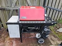 Full photo of red Weber Genesis gas grill showing side shelf, lid closed, and base with wheels and propane tank holder.
