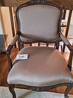 Front view of one arm chair showing carved wooden frame and striped upholstery on seat and backrest.