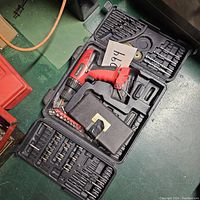 Photo showing red Stalwart corded drill in black plastic carrying case with assortment of drill bits, screwdriver bits, and brush wheels