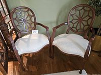 Two wood armchairs with spider back and cream seats shown side-by-side in a room