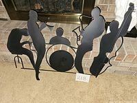 Photo shows black metal jazz band wall decor with silhouettes of four musicians: trumpet, drums, guitar, upright bass, placed on carpet in front of fireplace.