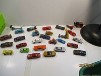 Wide shot showing all 28 Hot Wheels cars spread out on white surface with varied colors and designs.