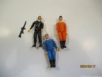 Three 3.75 inch A Team action figures: one in black tactical outfit, one in blue jumpsuit, one in orange jumpsuit, plus a separate black rifle gun accessory.