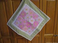 Full view of the baby quilt showing the square shape, pink and yellow floral block pattern, and green and white border.