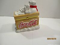 Front and side view of Coca-Cola collectible ceramic chest with polar bear and cubs figurine on top, highlighting painted details and logo.