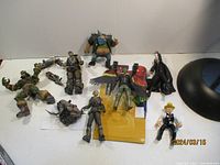 Photo showing ten assorted action figures on a white background, featuring a mix of styles, including a large colorful cartoonish figure with blue face and spiked armor warrior.